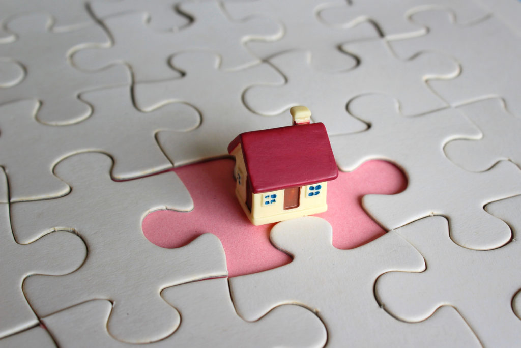 Concept of owning a home or completing a home purchase. Toy house and missing puzzle pieces.